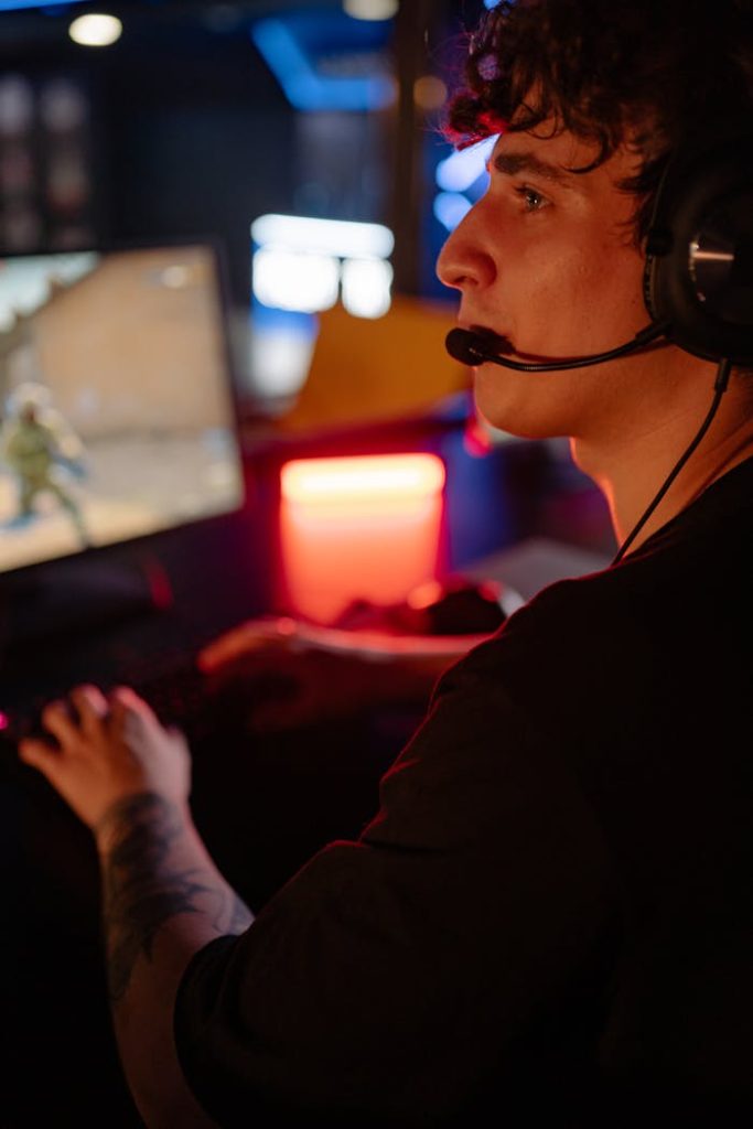 A young man wearing a headset engrossed in an online gaming match with colorful lights.