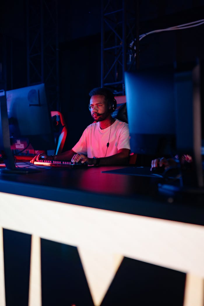 A young man intensely playing a PC game in a dimly lit esports arena.